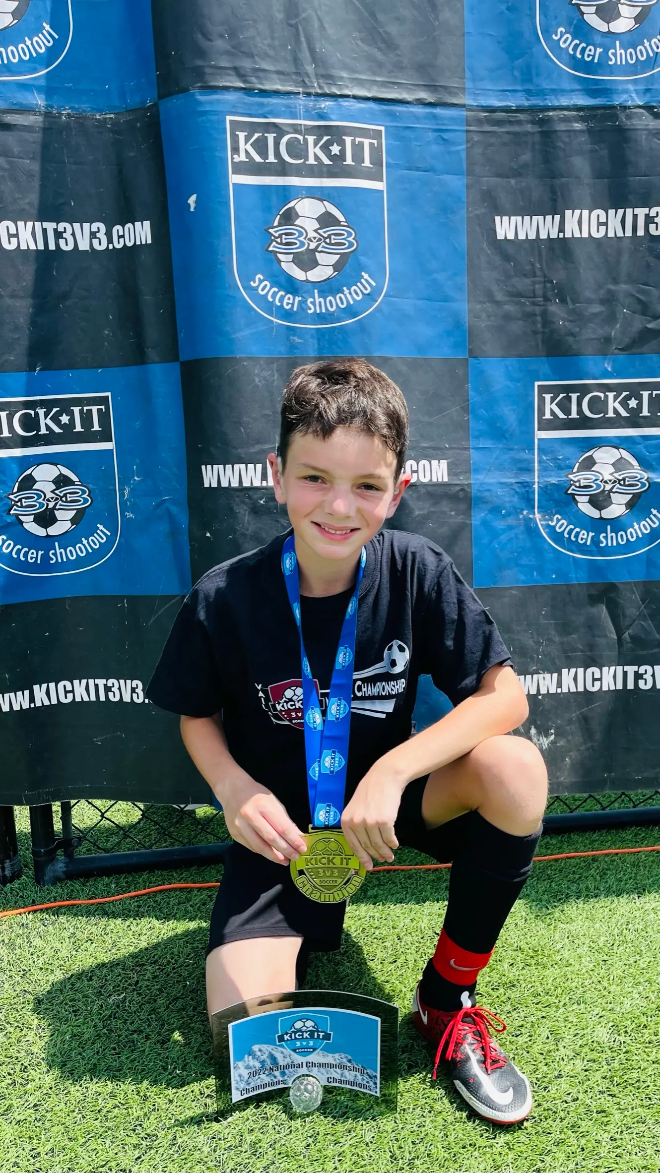 Daylen Hammon kneeling at Kick It 3v3 National Championship backdrop with gold medal and trophy 2022